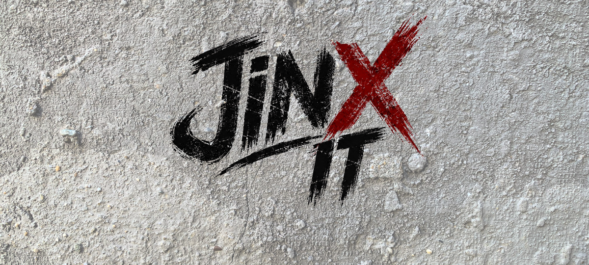 רקע JINX IT עם עיצוב X אדום על קיר בטון, כותרת WEAR THE CHAOS